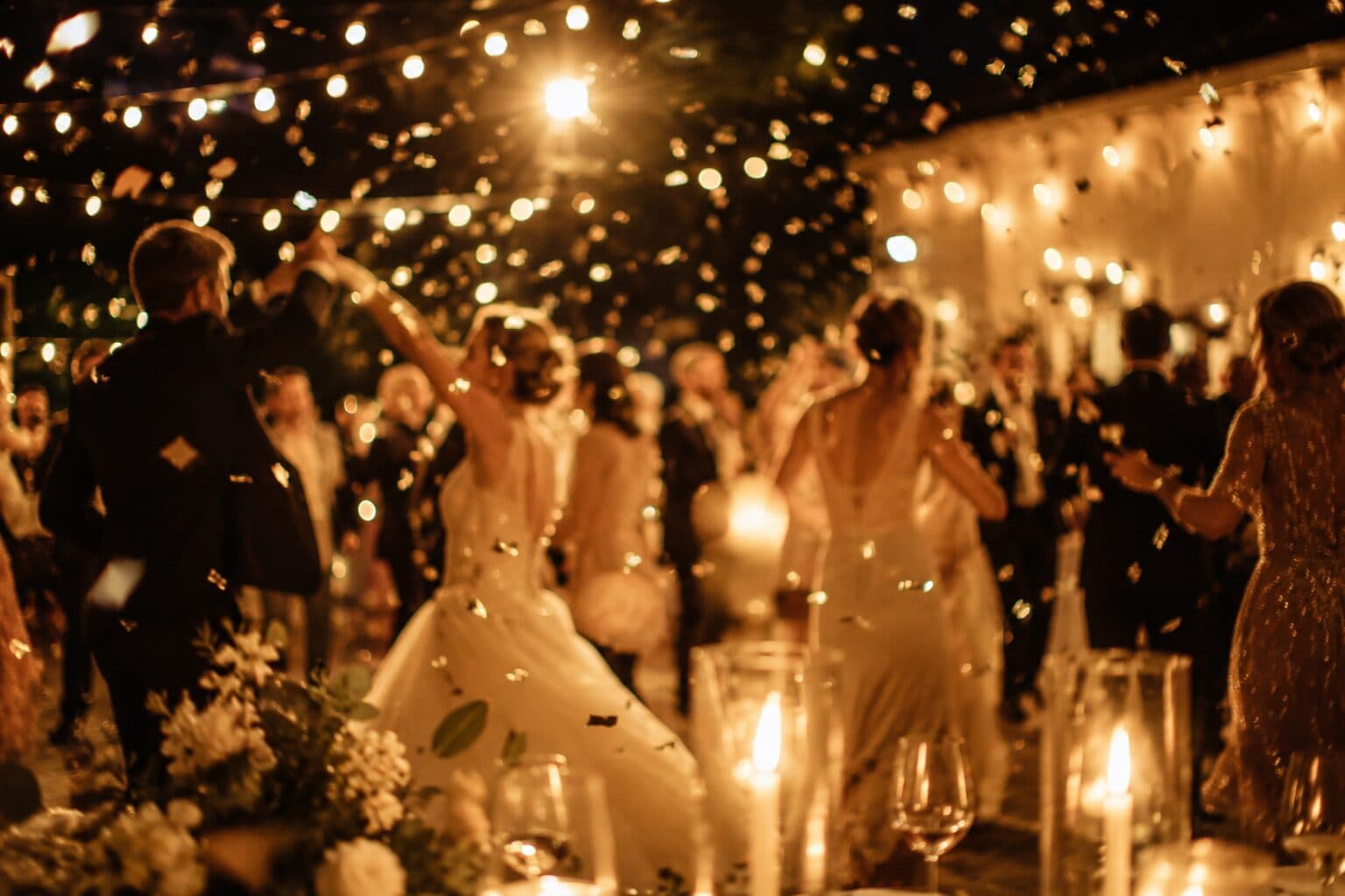 Goście tańczący wieczorem pod girlandami świetlnymi, w powietrzu confetti